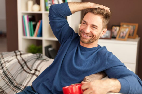 Hombre de buena densidad capilar peina su cabello con la mano mientras toma una taza de café