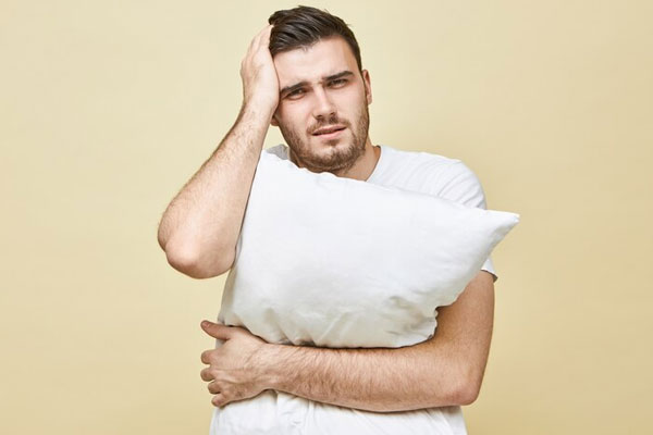 Insomnio afecta el pelo - Hombre con dolor de cabeza abraza una almohada en busca de soluciones para conciliar el sueño