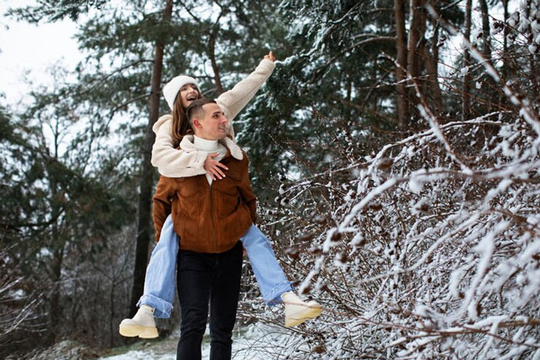 Cabello en invierno - Joven de cabello suelto va cargada sobre la espalda de su novio mientras dan un paso por el bosque 