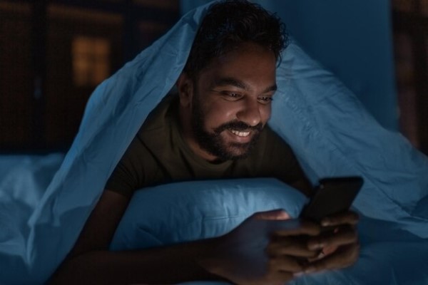 roncar provoca alopecia - hombre usando un móvil antes de dormir, lo cual puede causar un problema al dormir que incluya ronquidos
