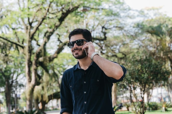 cortes de pelo - hombre sonriente con un buen corte de pelo paseando por el parque mientras habla por teléfono