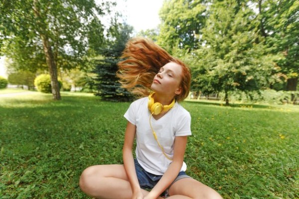 joven pelirroja con su melena suelta sin un solo accesorio para el pelo sentada en el césped de un parque