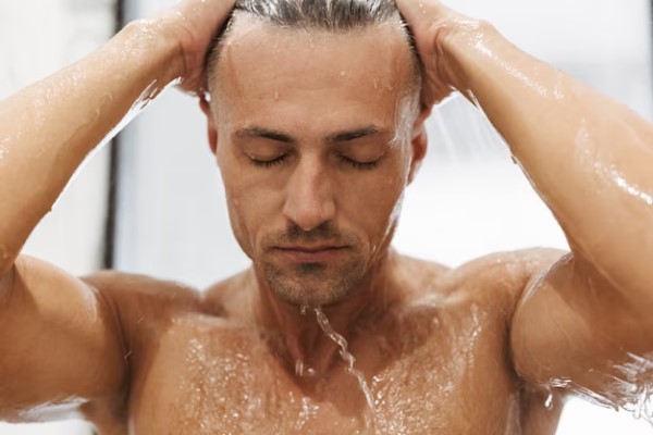 hombre lavando el cabello con agua tibia para no estimular la producción de grasa por el cuero cabelludo