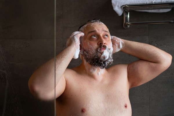 hombre en la ducha enjabonándose la cabeza para lavar su cabello grasoso