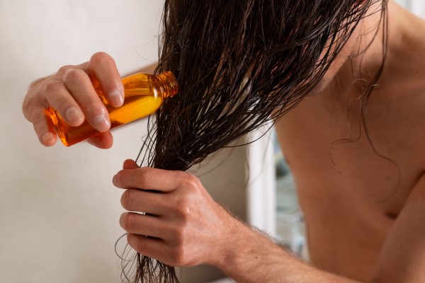 hombre aplicando aceites esenciales naturales a su cabello grasoso