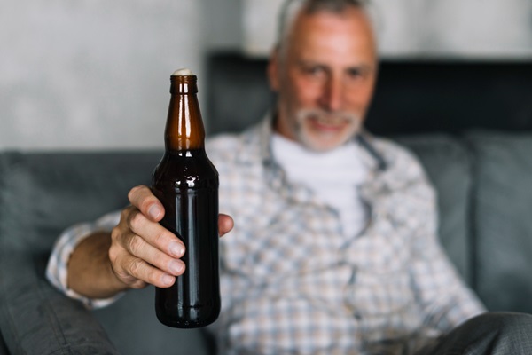 Alcohol en el injerto capilar - Hombre de cabello blanco muestra en su mano una botella de cerveza