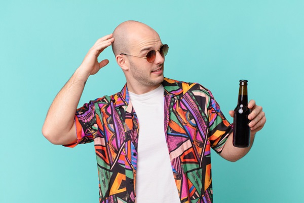 Alcohol en el injerto capilar - Hombre con alopecia tocándose la cabeza mientras sostiene en su mano una botella de cerveza
