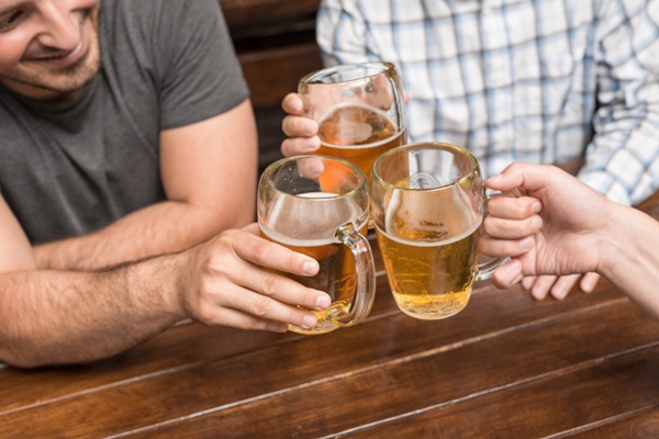 Grupo de hombres brindando con vasos de cerveza en una mesa de madera