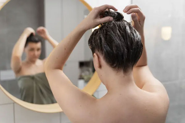Joven se recoge el cabello frente al espejo tras aplicarse una mascarilla de hidratación capilar