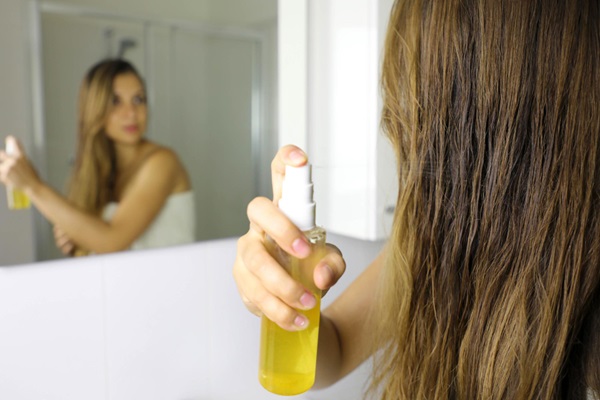 Aclarar el pelo - Mujer mirándose al espejo para aplicar un aceite en spray que aclara el pelo de forma natural