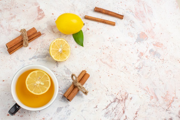 Taza con zumo de limón junto a varios limones y palos de canela para realizar una mascarilla capilar