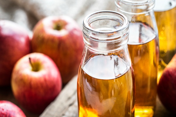Botellas con vinagre de manzana junto a varias manzanas rojas que ayudan a dejar el cabello brillante, suave y resistente