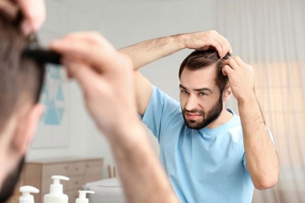 Alopecia prematura - Hombre con entradas y con pérdida de cabello se observa preocupado frente al espejo