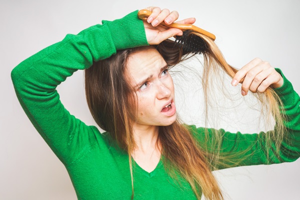 Mujer usando un cepillo para peinar el pelo dañado y con las hebras enredadas