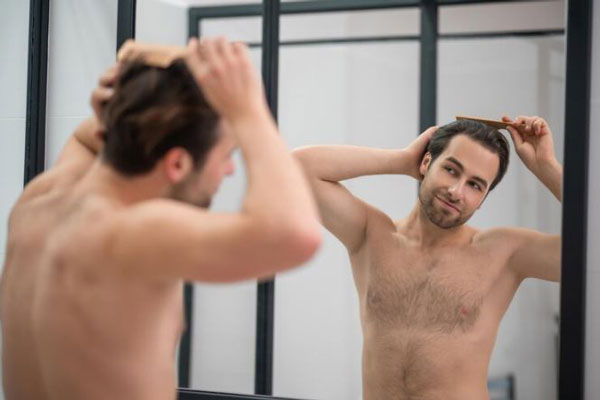Alopecia prematura - Hombre feliz cepilla su abundante cabellera frente al espejo