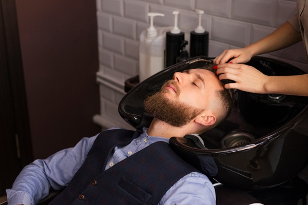 Masajes capilares - Hombre en una barbería recibiendo un masaje en el cuero cabelludo para eliminar las células muertas y el exceso de sebo