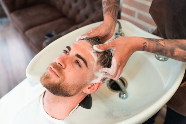 Masajes capilares - Barbero realizando un masaje capilar a un hombre con un champú revitalizante para frenar la pérdida de cabello
