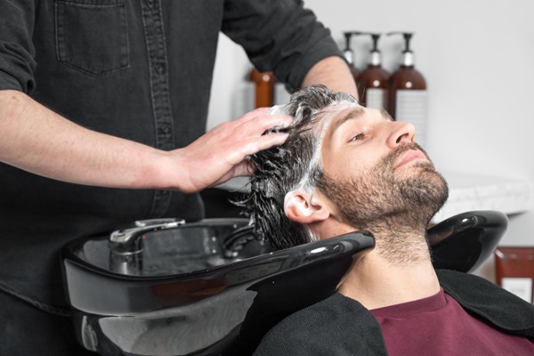 Estilista realizando un masaje en el cuero cabelludo mientras aplica champú para lavar el cabello de un hombre
