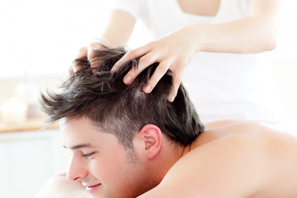 Hombre feliz y relajado mientras le hacen un masaje en la cabeza para frenar la caída del pelo