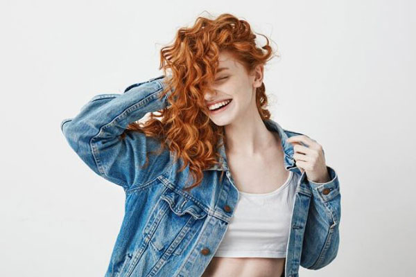 Peinar cada tipo de pelo - Joven peliroja de amplia sonrisa disfruta de su cabello rizado