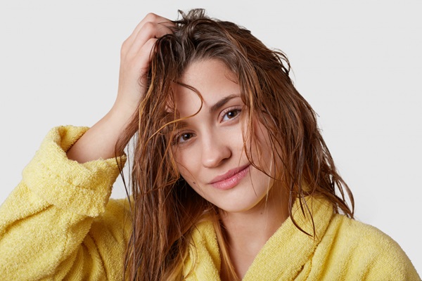Cómo cuidar el cabello mojado - Mujer sonriente tocando con su mano el pelo mojado mientras se seca al aire libre