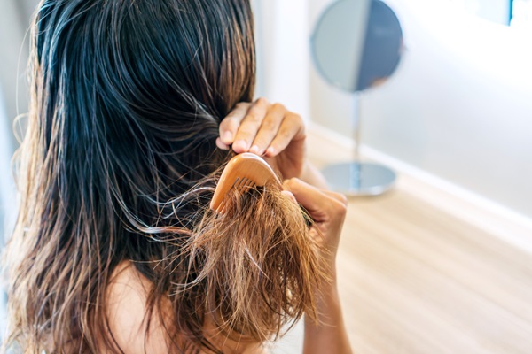 Cómo cuidar el cabello mojado - Mujer intentando desenredar el cabello mojado usando un cepillo, lo cual puede dañar el pelo y romper la fibra capilar