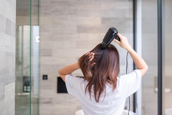 Mujer utilizando un secador eléctrico para eliminar el exceso de humedad y alisar el pelo
