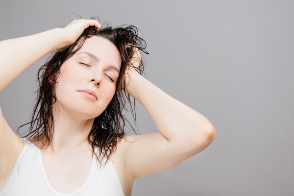 Mujer joven con los ojos cerrados poniendo sus manos en el pelo húmedo luego de una limpieza capilar