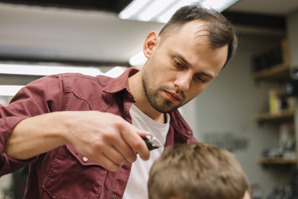 Cortar el cabello - Barbero usando una máquina de afeitar para cortar el pelo de un hombre