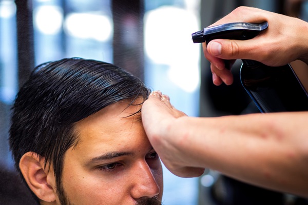 Barbero rociando con agua el pelo de un hombre para crear un peinado clásico y elegante