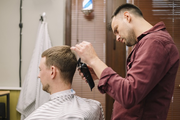 Peluquero usando una máquina de afeitar inalámbrica para realizar un corte clásico a un hombre