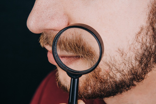 Hombre colocando una lupa en su rostro para observar el crecimiento del vello facial grueso luego de un implante de bigote y barba