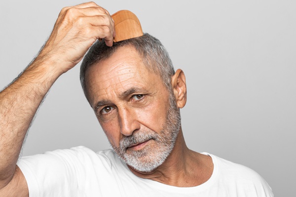 Injerto de pelo con canas - Hombre con pérdida de cabello en las entradas peinando su pelo canoso con un cepillo de madera