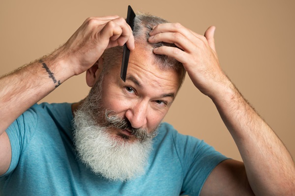 Injerto de pelo con canas - Hombre con alopecia y barba prominente peinando su cabello de color grisáceo debido a las canas