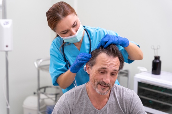 Médico especialista evaluando el cuero cabelludo de un hombre con alopecia para determinar las causas de la caída del cabello