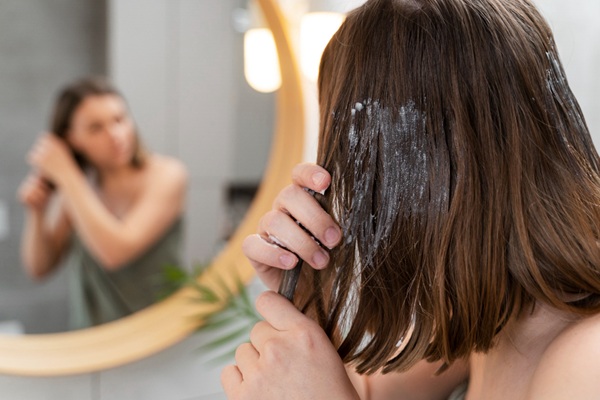 Trucos de cabello - Mujer frente al espejo aplicándose una mascarilla capilar hidratante para obtener un cabello brillante y sedoso