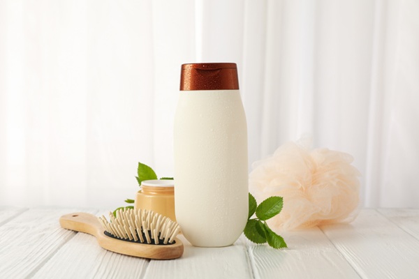 Trucos de cabello - Recipiente de champú junto a un peine y productos capilares sobre una mesa blanca