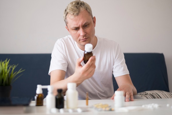 Vitaminas para evitar la alopecia - Hombre con pérdida de cabello leyendo un envase de vitaminas con varios suplementos vitamínicos sobre la mesa