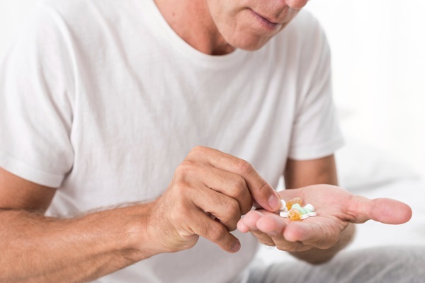 Hombre sosteniendo en su mano varias pastillas para seleccionar el suplemento vitaminico adecuado