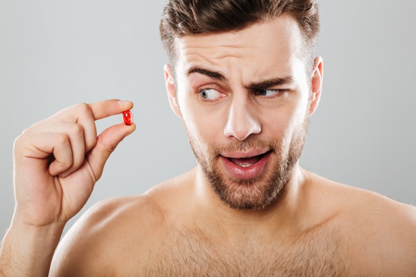 Vitaminas para evitar la alopecia - Hombre con cara de inquietud sosteniendo en su mano una pastilla de suplemento vitamínico