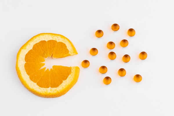 Vitaminas para evitar la alopecia - Rebanada de naranja junto a varias cápsulas de vitamina C que ayudan a reforzar el sistema inmunológico