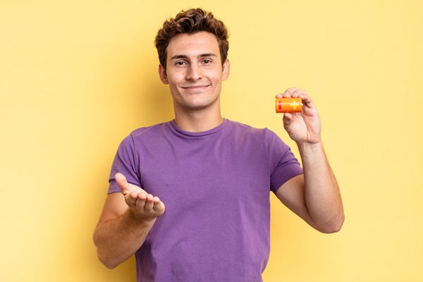 Hombre sonriente sosteniendo en su mano un recipiente de pastillas para suplemento de nutrientes