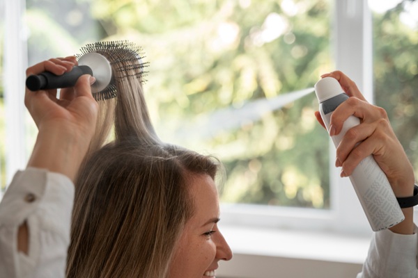 Cuidados para embellecer el cabello - Mujer joven utilizando un cepillo mientras aplica un producto capilar para crear un peinado con volumen