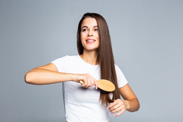 Cuidados para embellecer el cabello - Mujer peinando su pelo con un cepillo suave de madera para eliminar los nudos