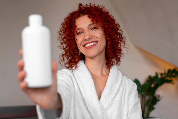 Cuidados para embellecer el cabello - Mujer pelirroja con rulos sosteniendo en su mano un recipiente de champú ideal para su tipo de cabello
