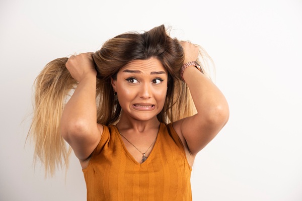 Mujer estresada con cara de desesperación jalando el cabello con sus manos siendo una de las causas del daño capilar