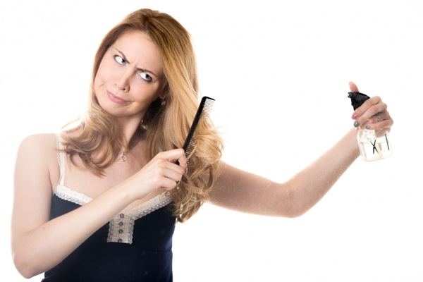 Mujer usando un peine y rociador mientras aplica un tratamiento capilar para eliminar el frizz y alisar el pelo