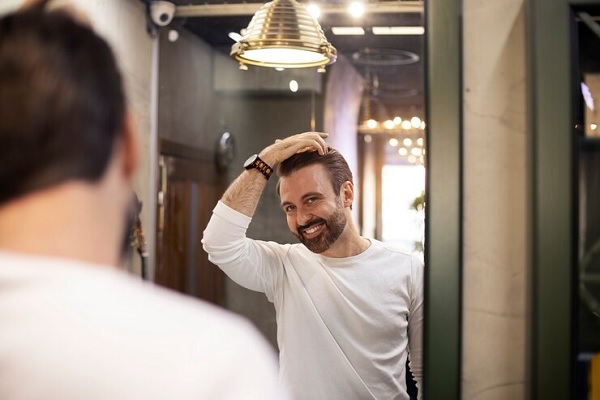 hombre mirando su cabellera frenta a un espejo, sonriendo