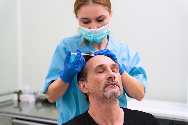 una especialista le realiza recibe un tratamiento para la pérdida de cabello a paciente masculino 