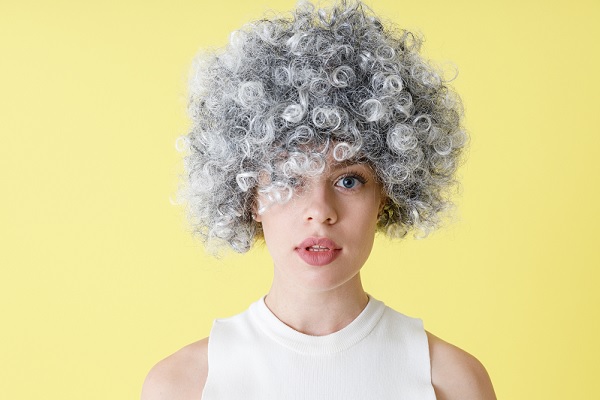 canas prematuras, una mujer joven con el pelo crespo y gris en un fondo amarillo